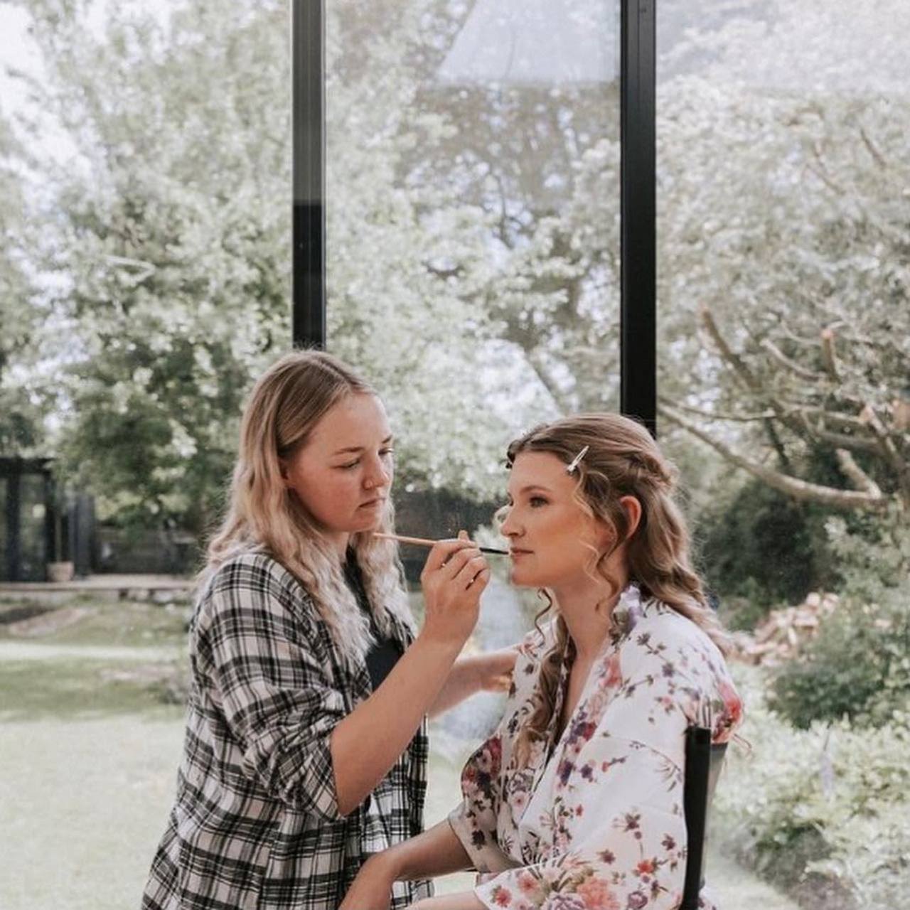 Charlie applying lip colour to a bride in a garden room at a wedding venue