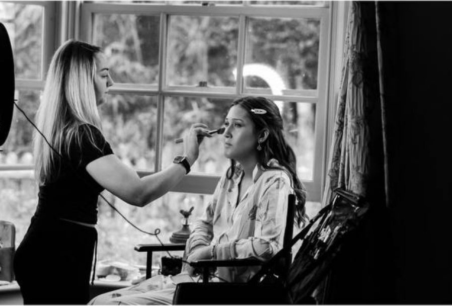 Black and white photo of Charlie doing bridal eye makeup by a window